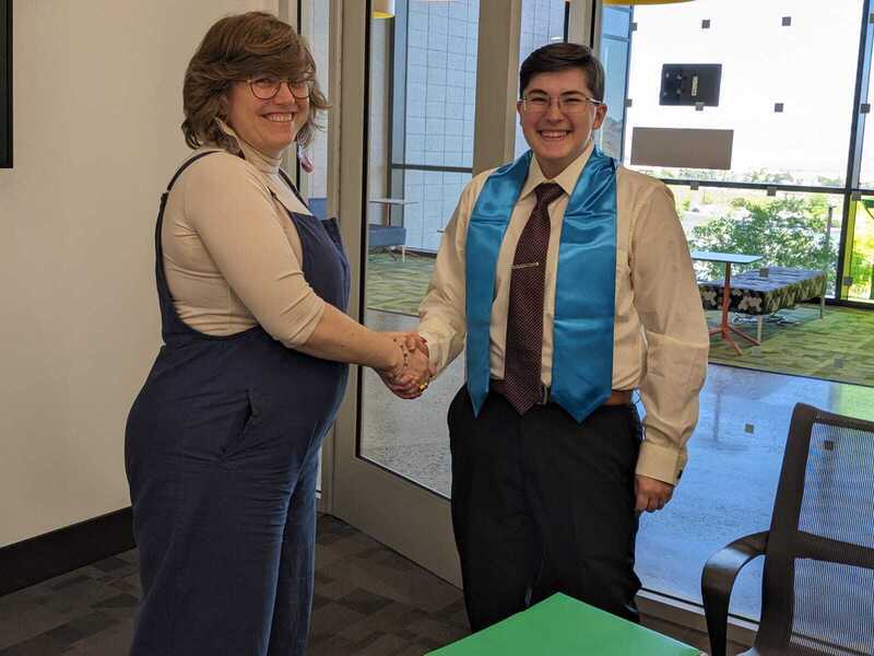 Photograph of Asa Baker wearing their honors stole, shaking hands with their advisor, Molly Appel.